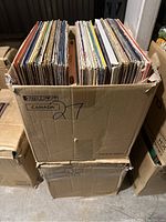 Top view of a cardboard box filled with vertically stored vinyl records with varied album covers showing.