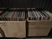 Two cardboard boxes filled with vinyl records labeled 35 and 36, showing the records upright with partially visible album covers and worn box edges.