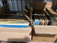 Two cardboard boxes filled with approximately 120 vinyl records, some album covers visible showing wear, colors, and text.