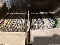 Two cardboard boxes filled with vinyl records seen from above showing records packed vertically with visible covers and spines.