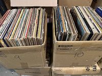 Two cardboard boxes densely filled with vinyl records, showing wear on album covers