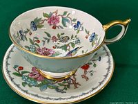 Top view of decorated Aynsley teacup and saucer with colorful floral and bird pattern and gold accents