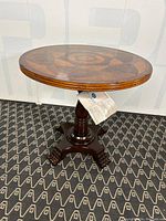 Full view of the round wooden inlay table showing the top surface, carved base, and claw feet.