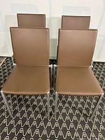 Front view of four brown leather dining chairs with metal legs on patterned carpet