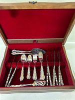 Wooden case with red velvet interior displaying cutlery pieces including forks, spoons, knives, and serving utensils.