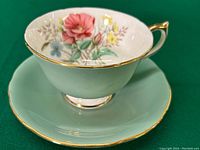 Front view of the teacup inside the saucer showing the floral painting and gold trim on the rim and handle.