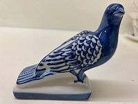 Blue and white ceramic bird figurine showing side profile with detailed painted feathers and glossy finish.