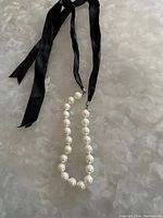 Full view of pearl necklace with black satin ribbon tie laid flat on a surface.