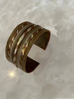 Wide cuff bracelet with mixed metal tones, viewed at an angle showing open end
