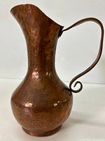 Front view of the copper pitcher showing its hammered texture and curved handle.