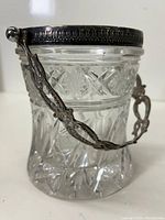 Side angle of the cut glass jar showing the detailed star etching and ornate metal handle with ball-end attachment to the jar.