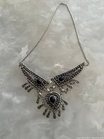 Full view of the silver-tone necklace featuring three pendants with black stones on a textured surface.