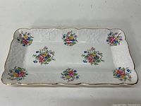 Rectangular white porcelain tray with floral bouquets and embossed edge pattern. Shows gold trim around scalloped edges.