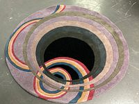 Top view showing full round carpet with black center and colorful rings on a concrete floor