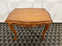 Front side view showing curved legs and carved floral detail beneath the tabletop.