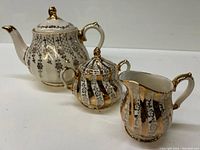 Front view of Sadler teapot, creamer, and sugar bowl set showing ornate gold and black pattern with gold accents.