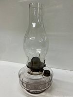 Frontal view of the old glass oil lamp showing the clear glass chimney, metal burner, and clear glass oil reservoir base.