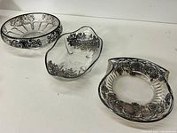 Set of three clear glass dishes with silver floral overlay displayed together on white surface.