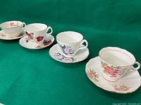 Four English teacups with matching saucers on green fabric background showing varied floral designs and gold trim.
