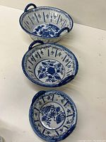 Three blue and white ceramic dishes arranged from largest to smallest, showing decorative floral patterns and handles