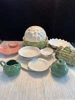 Photo of all cabbage and vegetable themed ceramic dishes and tableware together on light fabric surface with black background.