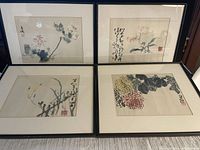 Set of four framed Chinese prints arranged in two rows of two on floor, showing overall lot condition and framing style.