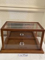 Straight front view of the wooden framed display box with glass panels and a wood base with mirror inlay.
