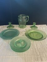 Photo shows the full lot of green glassware including pitcher, plates and candlesticks