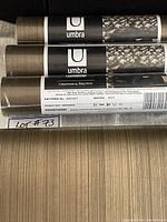 Three rolls of bronze Umbra Graham & Brown wallpaper with labels and partially unrolled wallpaper showing textured linear pattern.