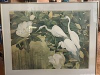 Full view of framed print showing pelicans among large flowers by a pond.