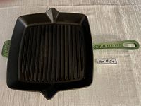 Top down view of square Staub green cast iron griddle showing black ridged cooking surface and long handle stamped STAUB.