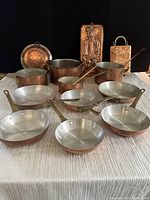 Front view showing six frying pans and cookware arranged on table