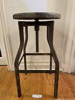 Side view of the vintage adjustable metal stool showing the curved legs, threaded central support for height adjustment, and worn metal finish.