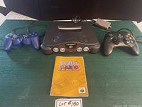 Nintendo 64 console with two controllers (blue and black) and Paper Mario instruction booklet on table.