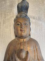 Close-up front view of figure’s torso and head showing carved detail and gilt wear