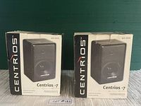 Two boxed Realistic Centrios 7 bookshelf speakers, boxes show signs of wear but speakers are reportedly new in box.