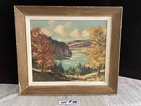 Framed oil painting showing Lac Rolland with fall foliage and river under partly cloudy sky.