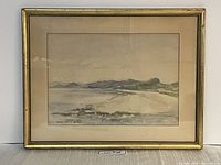 Framed watercolour painting showing a coastal scene with hills in the background and shoreline with water in the foreground.