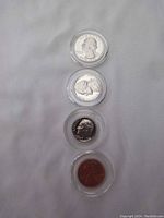 Four proof coins (quarter, nickel, dime, penny) displayed in a vertical row from top quarter to bottom penny, each encapsulated in clear circular holders to protect coins.