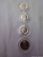 Set of four 1983 U.S. proof coins including quarter, nickel, dime, and penny in airtight clear plastic holders arranged vertically.