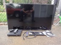 Photo of TCL 42-inch flat screen TV with Sony DVD player, remotes, HDMI cable, power adapter and wall-mount components arranged in front of the TV.