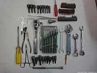 Full assortment of hand tools displayed on a white surface including ratchet, breaker bar, wrenches, bits, pliers, scissors and screwdrivers.