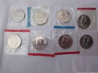 Eight Kennedy half dollars sealed in individual plastic mint cellophane packages, showing the front profile of President John F. Kennedy.