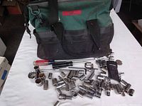 Overview of green Craftsman canvas tool bag with many chrome sockets and hand tools spread out in front of it