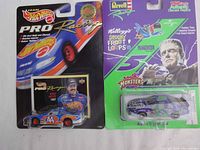 Photo showing the two diecast cars in original packaging side by side; left is the Hot Wheels Kyle Petty model with trading card; right is the Revell Racing Kellogg's Spooky Froot Loops themed car.