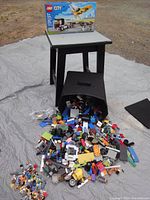 Photo of LEGO building table, boxed LEGO City aircraft and transport set on top, spilled container of LEGO pieces and minifigures in front