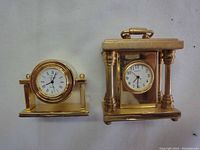 Front view of two brass miniature clocks showing different styles and dial designs.