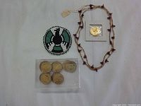 Overview of all items in the lot: a beaded hair barrette, beaded necklace, gold-colored medallion in plastic sleeve, and six arcade tokens.