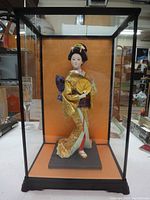 Front view of porcelain Japanese doll in the glass display case, showing full figure and traditional attire