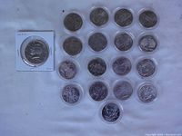Top view of 18 uncirculated U.S. statehood quarters in airtight plastic holders arranged on a surface alongside one Kennedy half dollar in a cardboard holder.